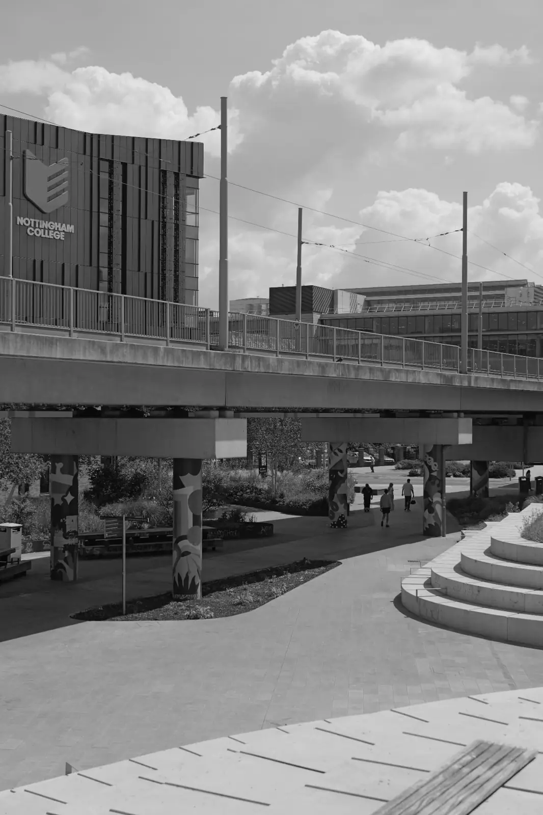 Nottingham tram lines running beneath a concrete overbridge with city buildings behind